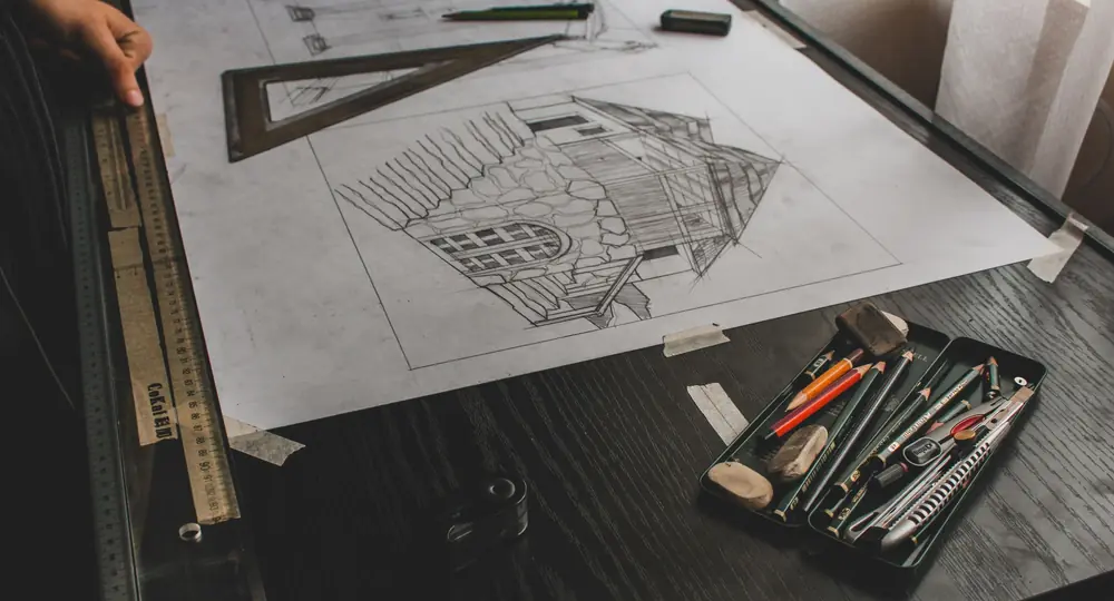 Pencil elevation on a drafting board beside a set square, rulers and pencils on a dark desk