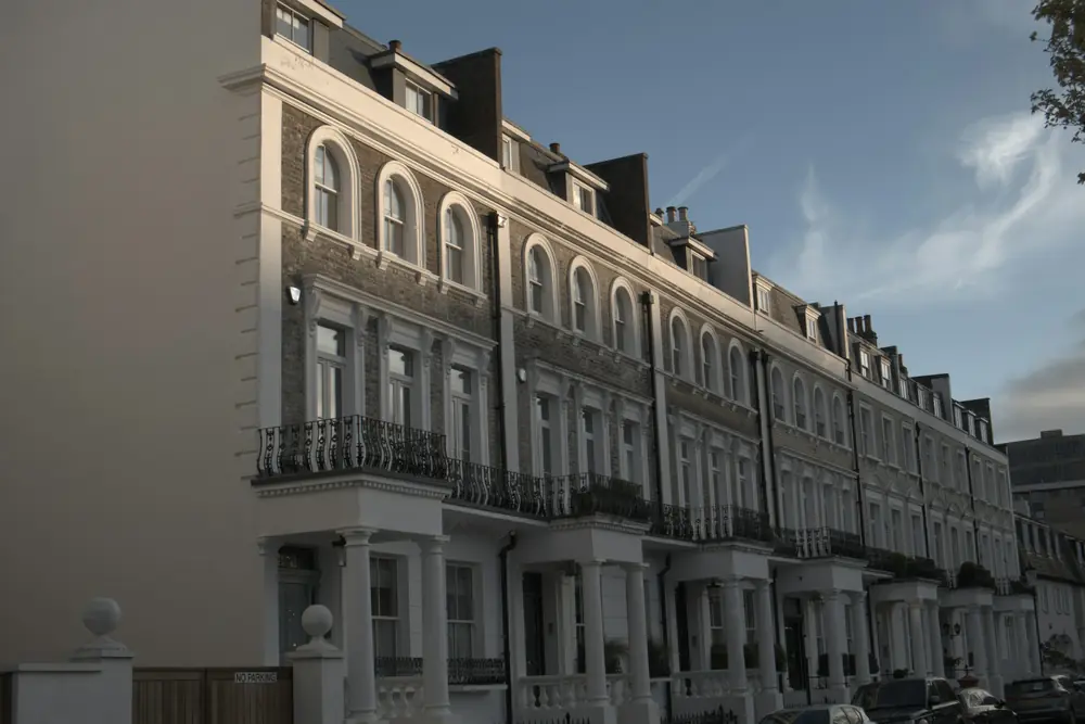Pale stucco terrace of Georgian-style houses with arched windows and iron balconies, lit by low evening sun on a Kensington street