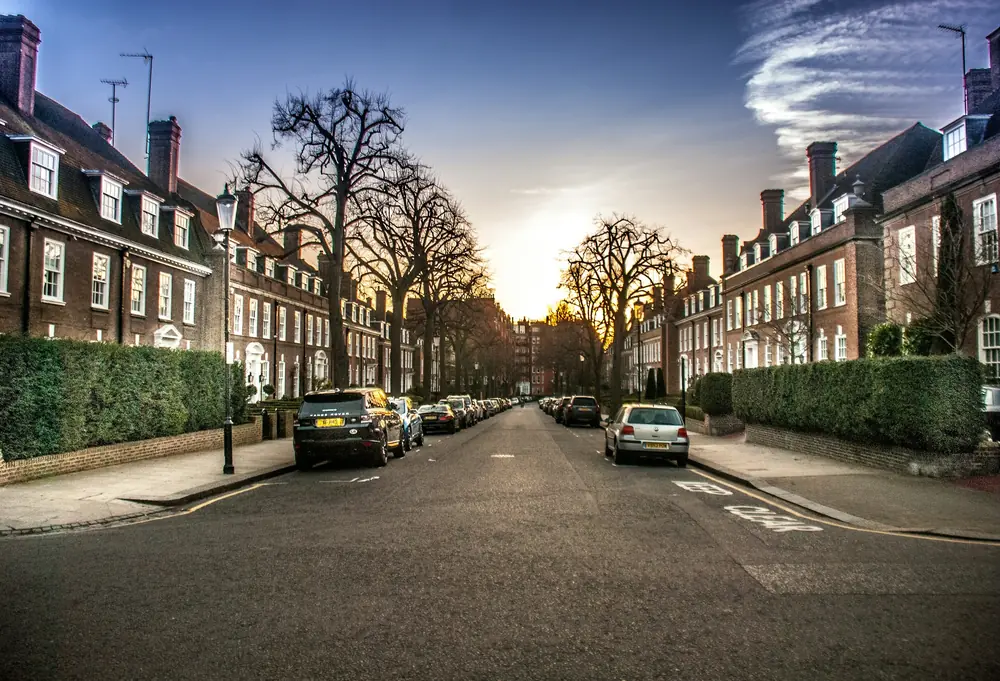 Kensington street lined with brick townhouses and lit streetlamps beneath an orange dusk sky
