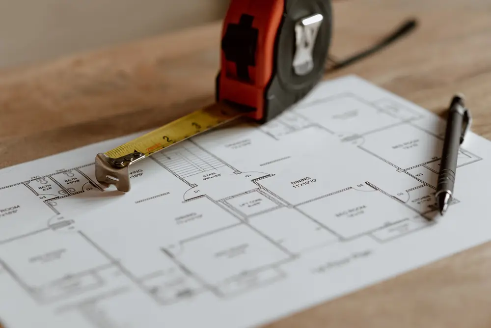 Tape measure and pen lying on a printed first-floor plan on a wooden table