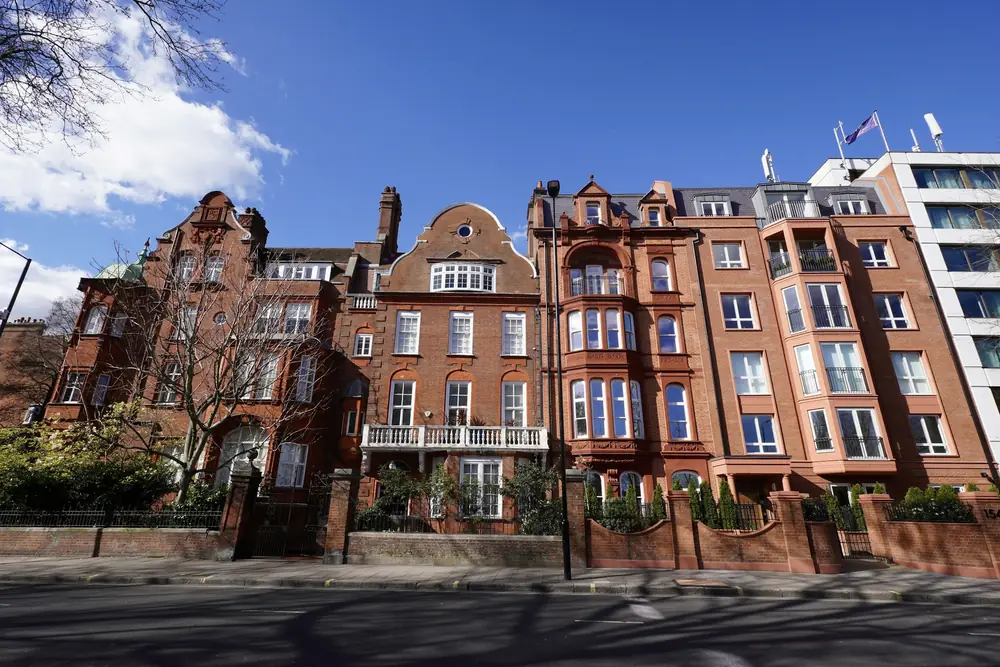 Tall red-brick Victorian houses on a Kensington street, with white balconies, gables and walled front gardens